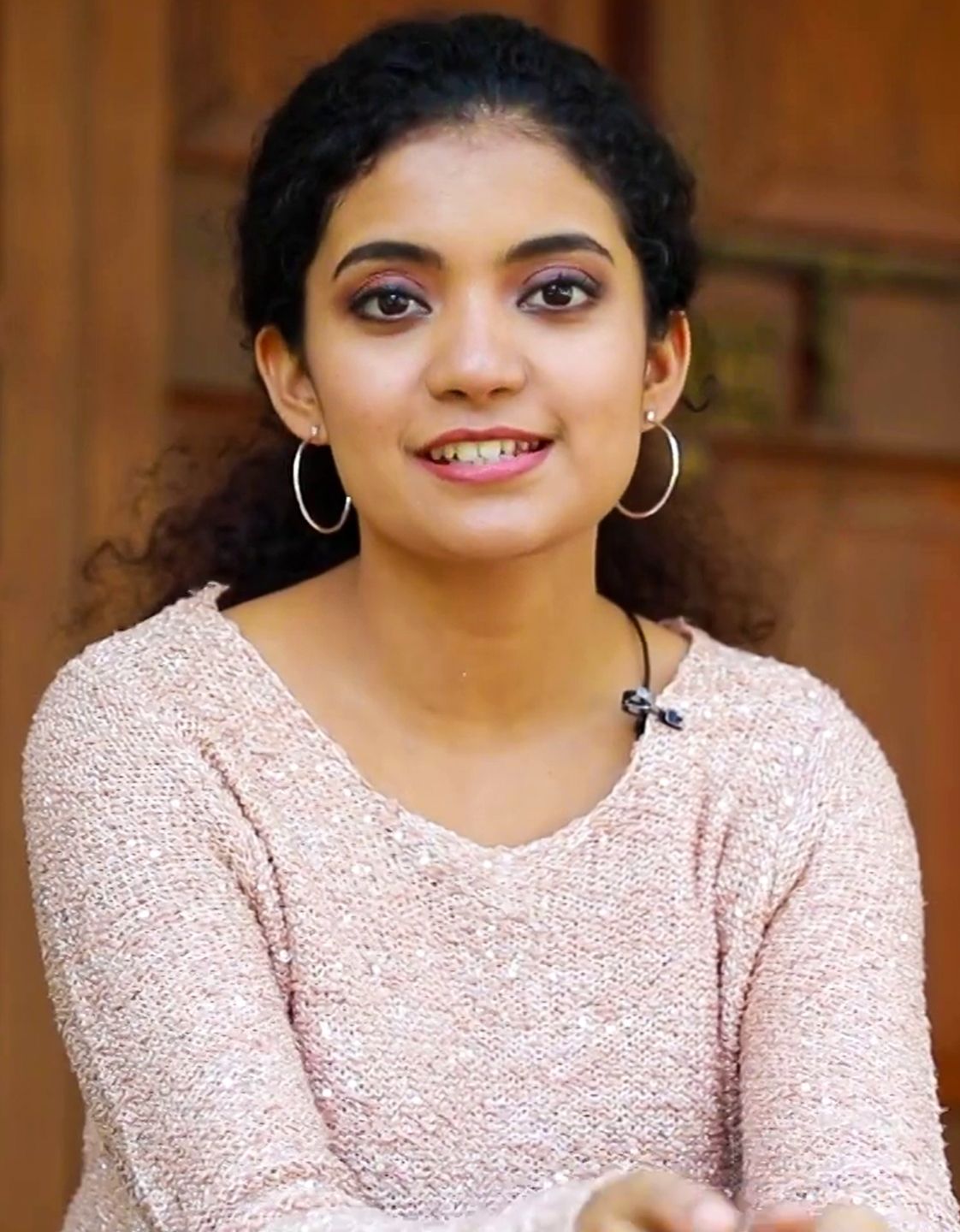 Anna Ben smiling in a pink sweater, wearing hoop earrings