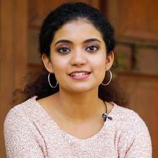 Anna Ben smiling in a pink sweater, wearing hoop earrings