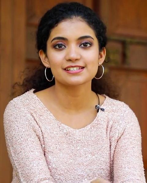Anna Ben smiling in a pink sweater, wearing hoop earrings