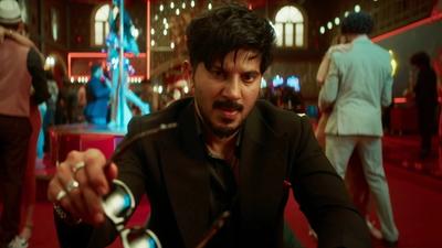 Dulquer Salmaan as Dan John holding out a pair of sunglasses in a casino in I'm Game