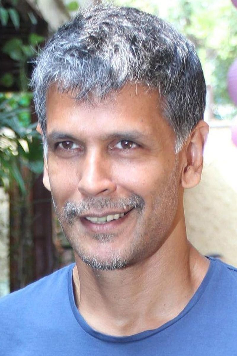 Milind Soman with grey hair smiling in a blue T-shirt