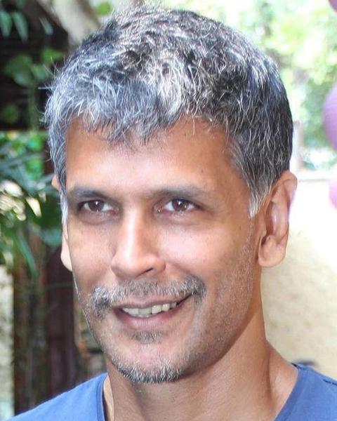 Milind Soman with grey hair smiling in a blue T-shirt
