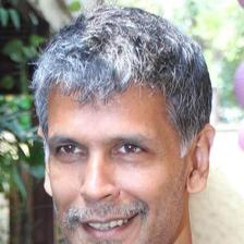 Milind Soman with grey hair smiling in a blue T-shirt