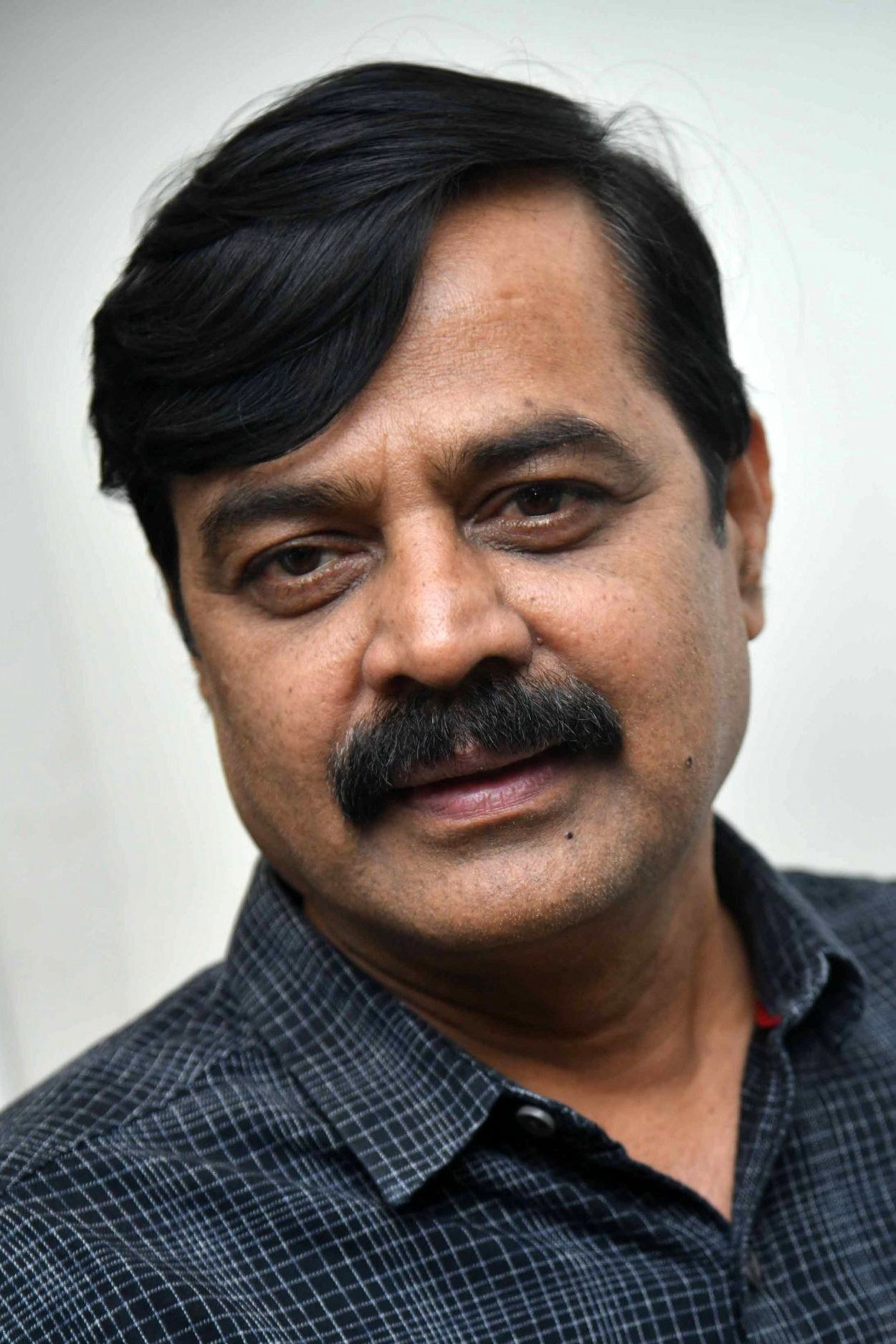 Achyuth Kumar with a moustache in a dark checked shirt, close-up portrait