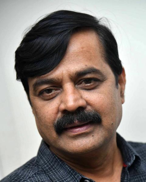 Achyuth Kumar with a moustache in a dark checked shirt, close-up portrait