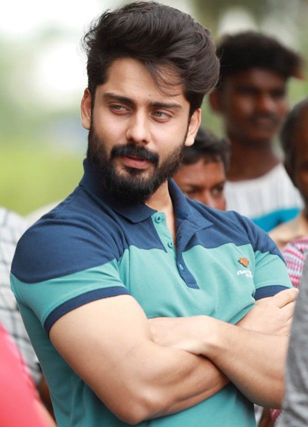 Roshan Basheer with a full beard, in a teal and navy polo shirt, arms folded outdoors