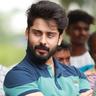 Roshan Basheer with a full beard, in a teal and navy polo shirt, arms folded outdoors