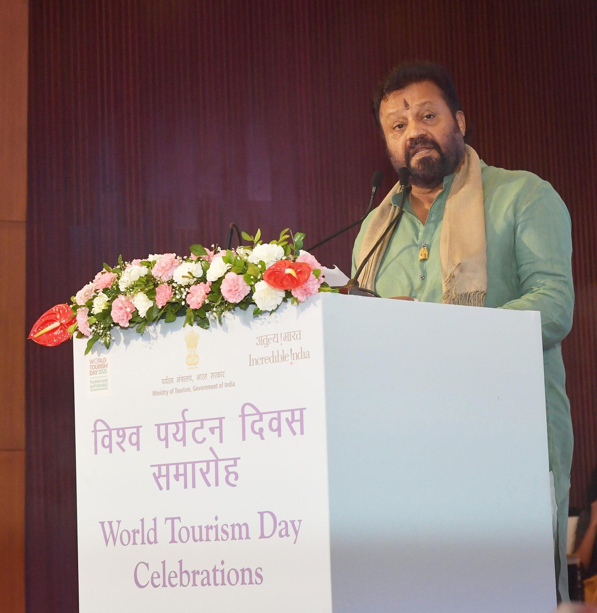 Suresh Gopi in a green kurta and shawl speaking at a World Tourism Day lectern