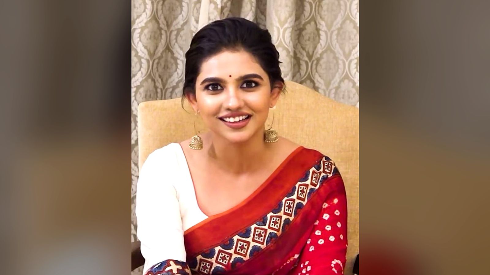Mamitha Baiju smiling in a white and red saree