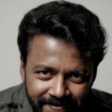 Vishnu Unnikrishnan with a beard in a dark jacket over a white T-shirt, grey backdrop portrait