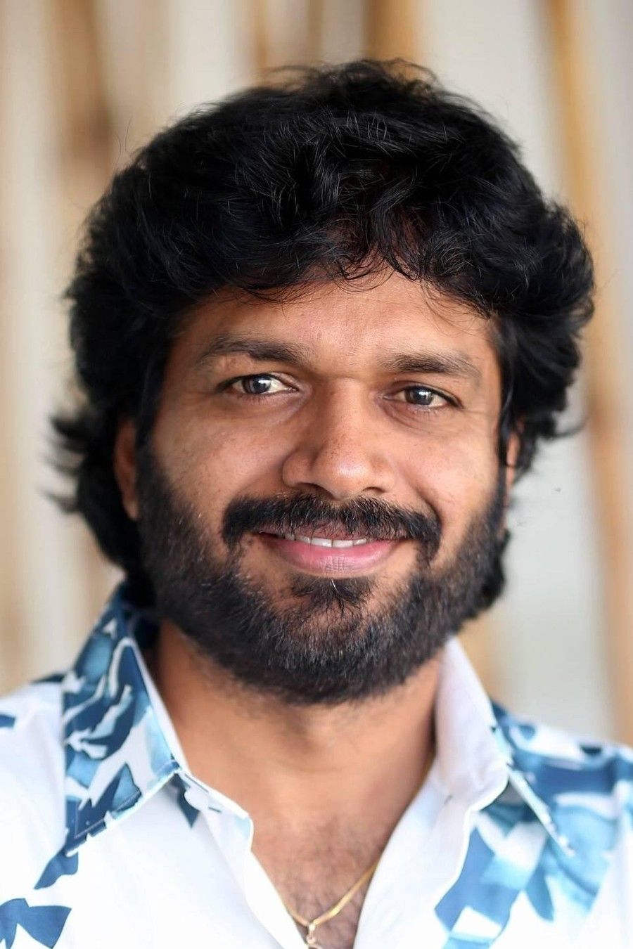 Anil Ravipudi with curly hair and a beard in a printed shirt, smiling