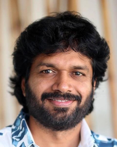 Anil Ravipudi with curly hair and a beard in a printed shirt, smiling