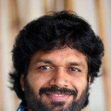 Anil Ravipudi with curly hair and a beard in a printed shirt, smiling