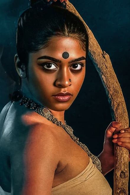 Asthikkari first look showing Sakhi Satya in character, with a black bindi and beaded necklace, gripping a curved wooden staff against a smoky dark background