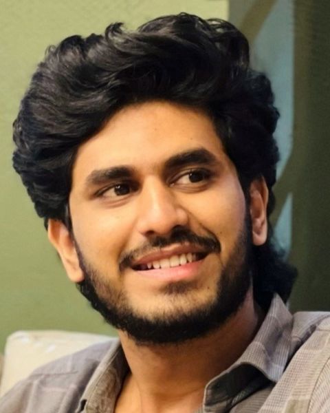 Nihal Nizam smiling and looking to the side in a grey checked shirt, head-and-shoulders portrait