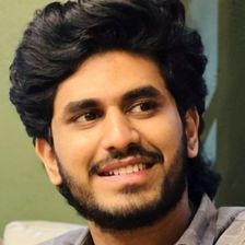 Nihal Nizam smiling and looking to the side in a grey checked shirt, head-and-shoulders portrait