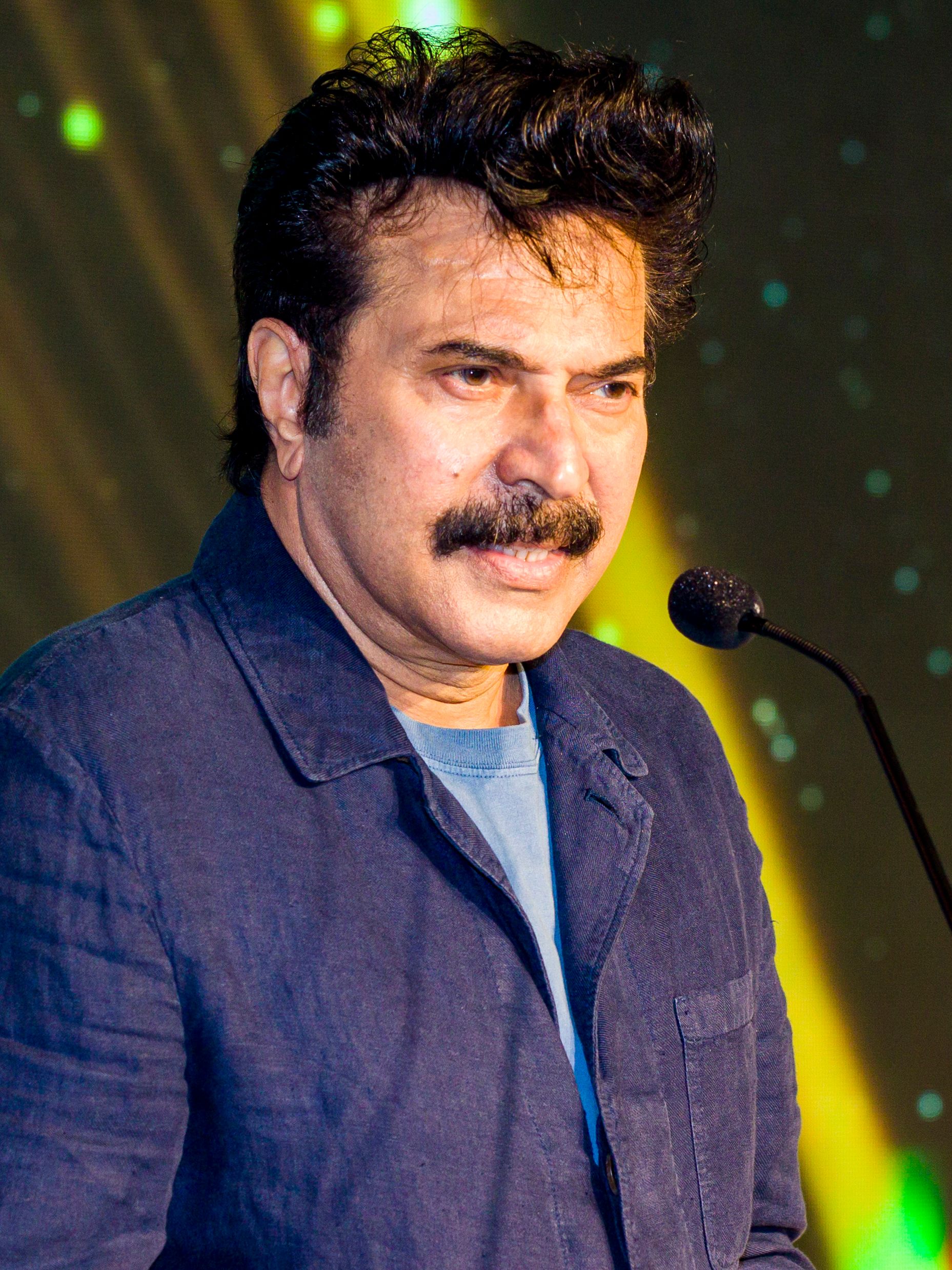 Mammootty speaking at a microphone in a blue denim jacket, 2022