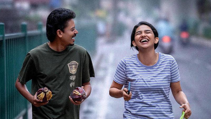 Sangeeth Prathap and Mamitha Baiju laughing as they walk down a wet street in the Hello Dear release date poster