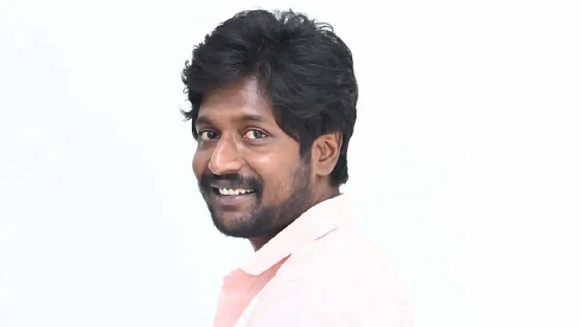 Suhas smiling in a pink shirt against a light background