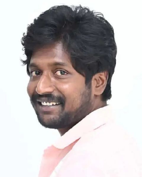 Suhas smiling in a pink shirt against a light background