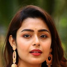 Mokksha in gold jhumkas and a white top against green foliage, portrait