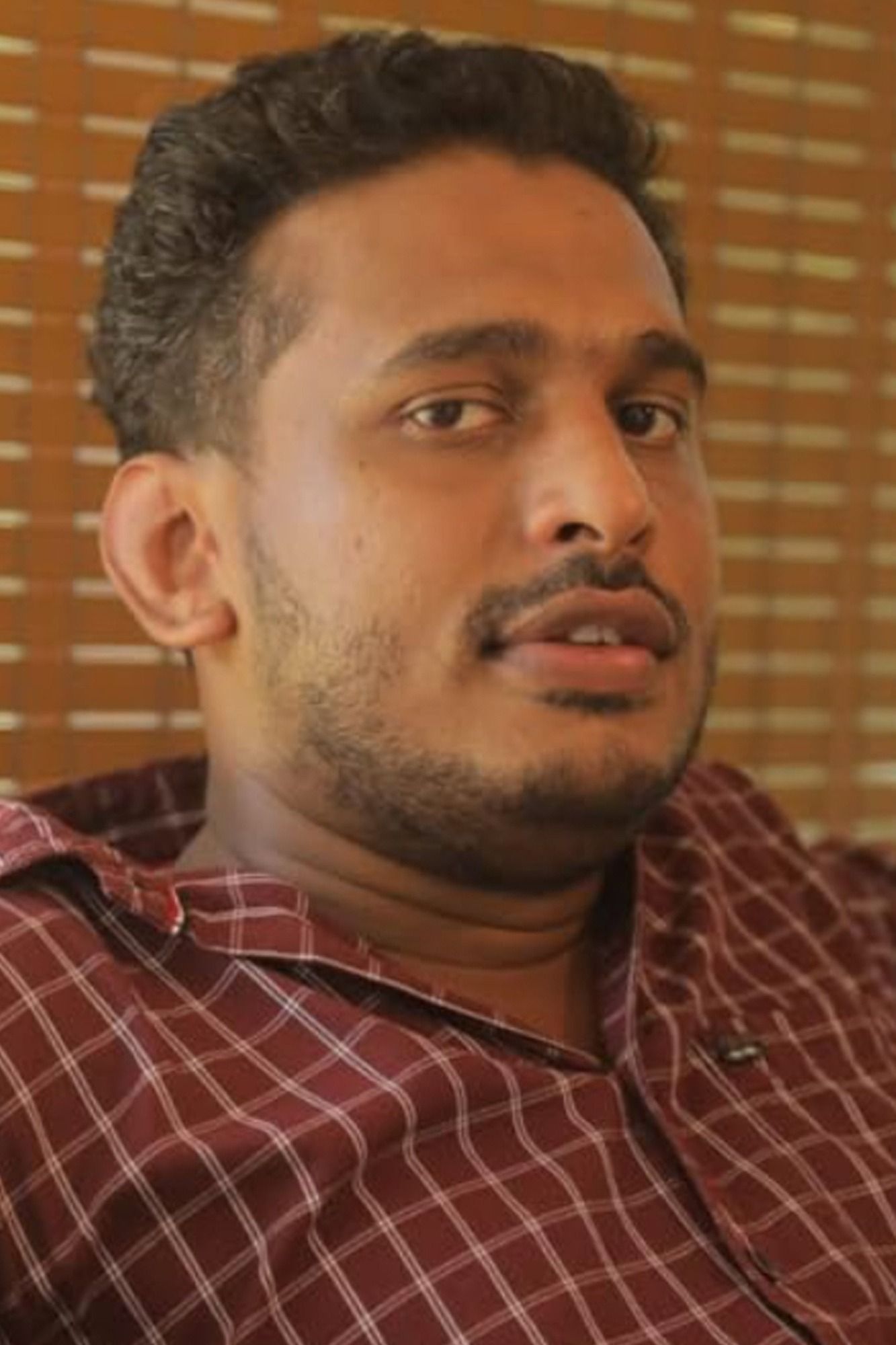 Girish A. D. in a checked shirt glancing to the side, close-up