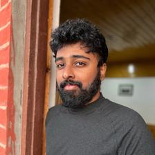 Nimish Ravi in a grey sweater leaning against a red door frame