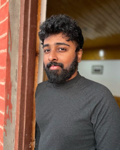 Nimish Ravi in a grey sweater leaning against a red door frame