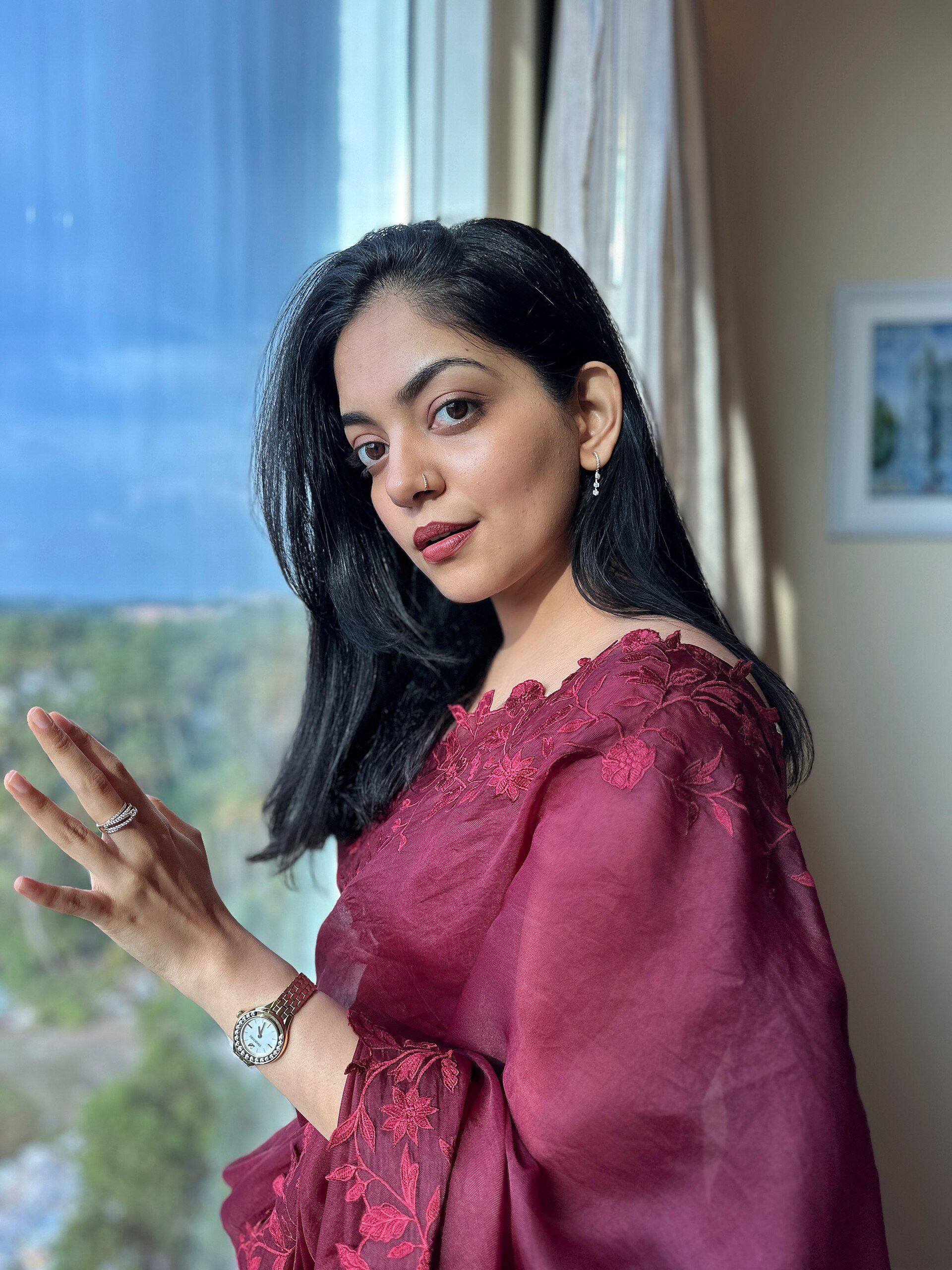 Ahaana Krishna in a maroon saree, three-quarter portrait by a window