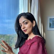 Ahaana Krishna in a maroon saree, three-quarter portrait by a window