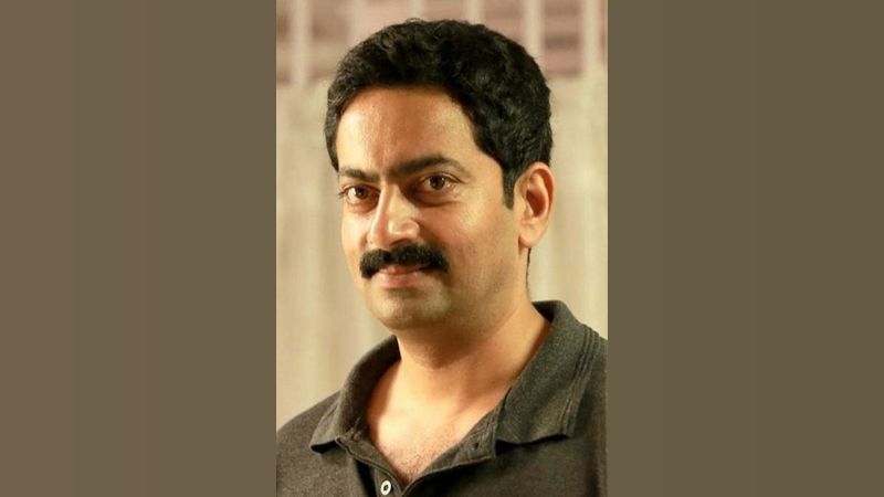 Saiju Kurup in a dark grey polo shirt, smiling slightly at the camera