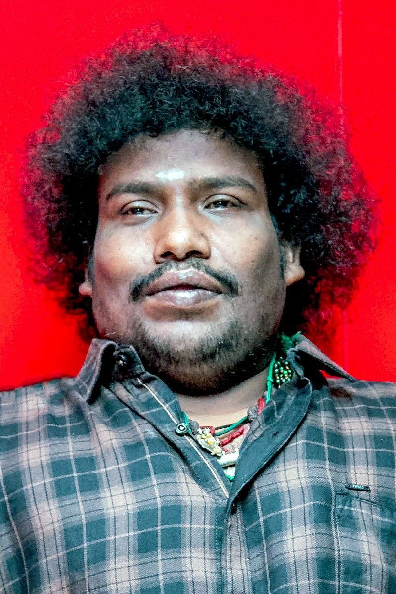 Yogi Babu with curly hair in a checked shirt against red