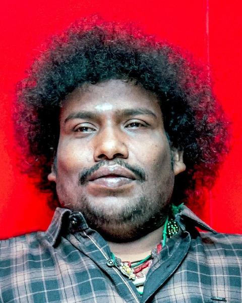 Yogi Babu with curly hair in a checked shirt against red