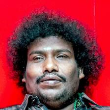 Yogi Babu with curly hair in a checked shirt against red