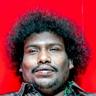 Yogi Babu with curly hair in a checked shirt against red