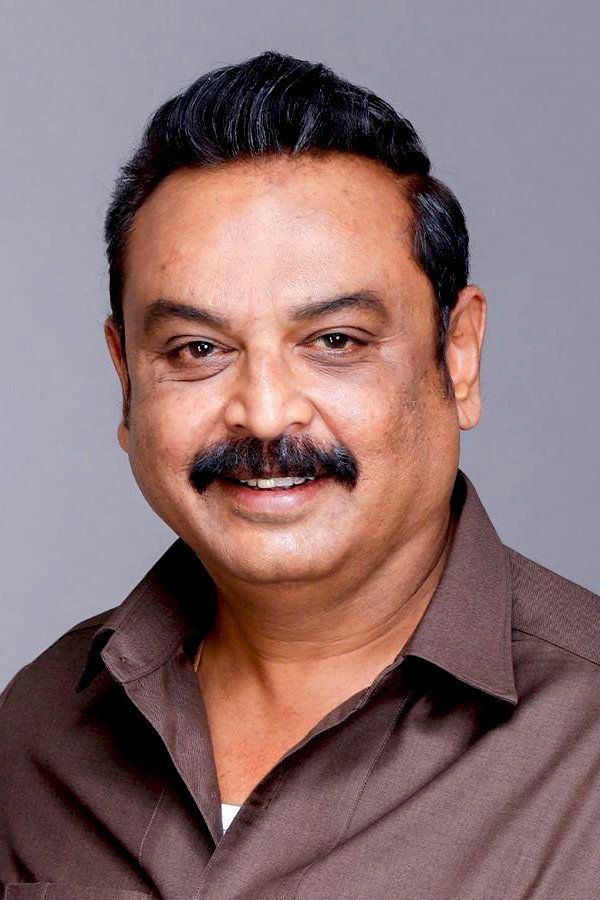 Telugu actor V. K. Naresh with a moustache, in a brown shirt, smiling in a studio portrait