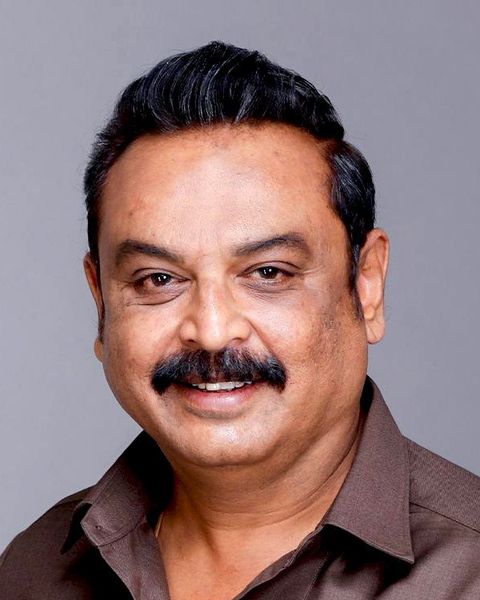 Telugu actor V. K. Naresh with a moustache, in a brown shirt, smiling in a studio portrait