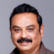 Telugu actor V. K. Naresh with a moustache, in a brown shirt, smiling in a studio portrait