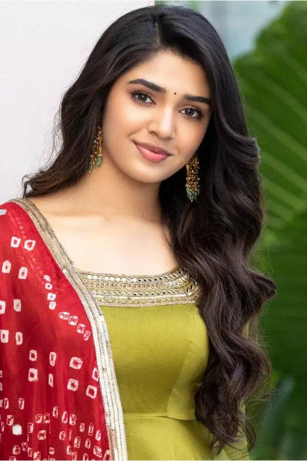 Krithi Shetty with long dark hair in a red dupatta and lime green kurta, smiling