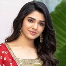 Krithi Shetty with long dark hair in a red dupatta and lime green kurta, smiling