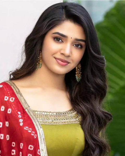 Krithi Shetty with long dark hair in a red dupatta and lime green kurta, smiling