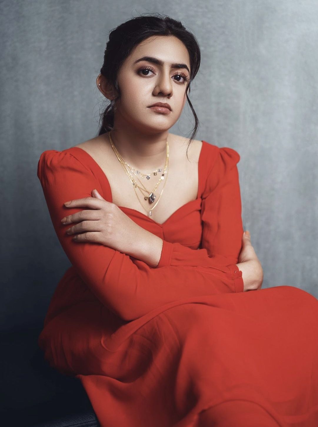 Femina George in a red dress seated against a grey backdrop