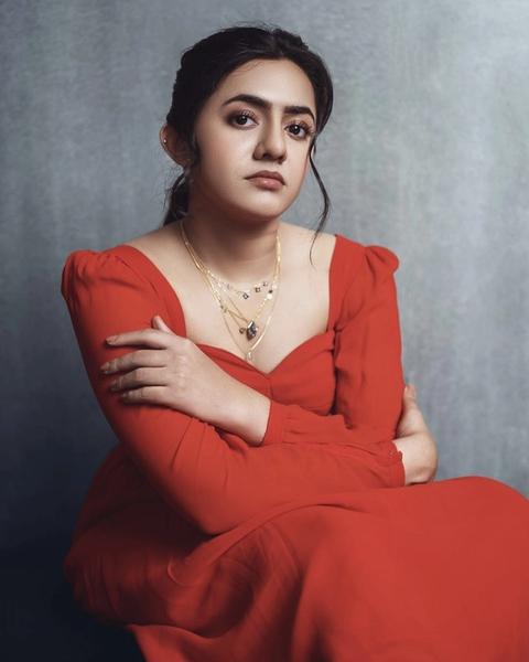 Femina George in a red dress seated against a grey backdrop
