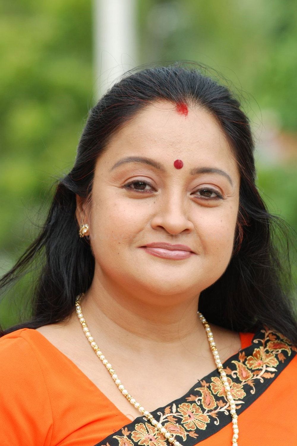 Geetha Vijayan smiling in an orange saree with a red bindi