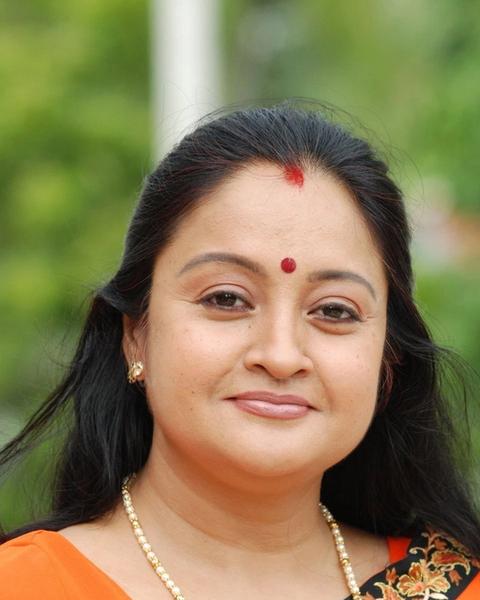 Geetha Vijayan smiling in an orange saree with a red bindi