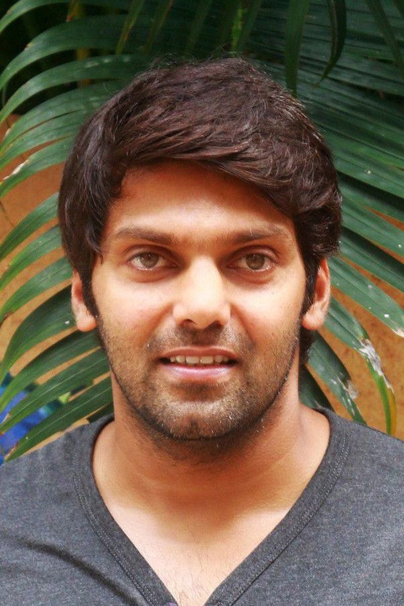 Arya smiling in a grey T-shirt in front of green palm leaves