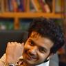 Sreenath Bhasi smiling with his hand raised, seated portrait