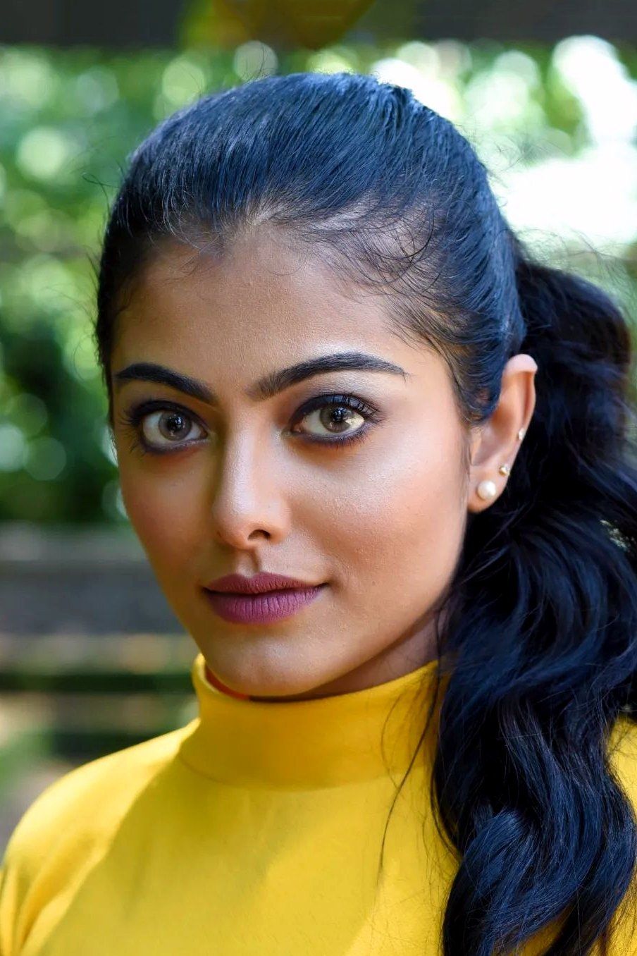 Merin Philip in a yellow high-neck top with her hair pulled back, green background portrait