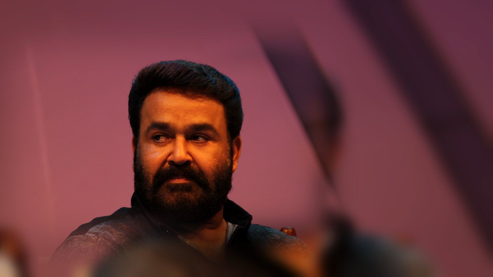 Mohanlal in a dark shirt, looking to the side at an event