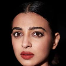 Radhika Apte with her hair pulled back and red lipstick against a black background, portrait